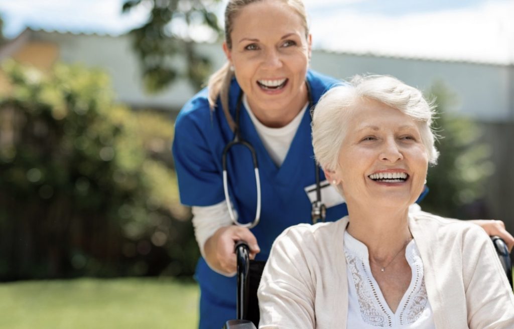 Smiling Nurse Pushing a Happy Senior on a Wheelchair Bigger